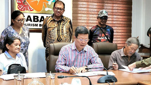 Sabah Tourism Board’s Joniston Bangkuai Noredah Othman (standing, middle) witnessing the signing of MoU between Borneo Eco Tours’ Albert Teo (seated, middle) and villagers.